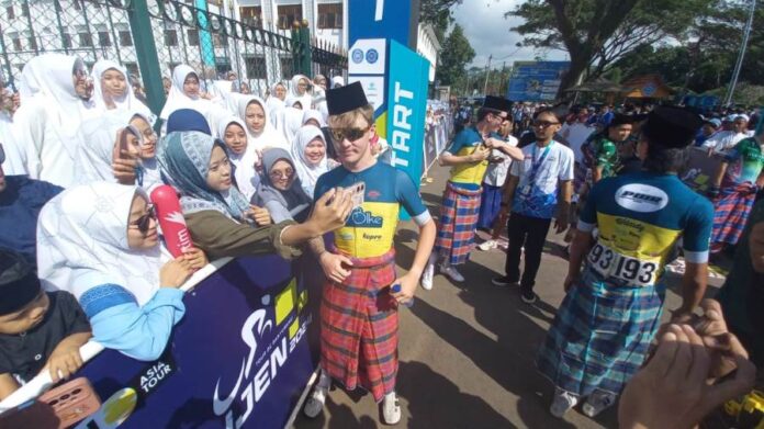WhatsApp Image 2024-07-22 at 05.39.21 Pembalap asing TdBI 2024 menggunakan sarung dan songkok berfoto bersama warga di start etape pertama, Senin (22/7/2024). (Foto/udi)